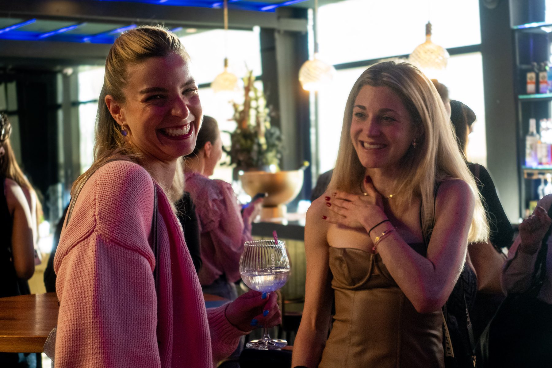 Two Playhard girls laughing together over drinks at a Zurich evening